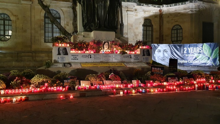 Schon kurz nachdem Daphne Caruana Galizia ermordet wurde, begannen ihre Familie und Angehörige der Zivilgesellschaft Blumen, Kerzen, Porträts und Plakate auf den untersten Stufen des Great-Siege-Denkmals in Valletta niederzulegen. In den englischsprachigen, maltesischen Medien war seitdem stets vom „makeshift memorial“, von der provisorischen Gedenkstätte für die durch ein Bombenattentat getötete Journalistin die Rede. Direkt gegenüber dem Justizpalast gelegen, war die improvisierte Gedenkstätte bisher  eine permanente Mahnung an die Justiz, den Fall vollständig aufzuklären. Diese Aufklärung scheint jetzt voran zu kommen, mit schockierenden Ergebnissen. In der Nacht zum Republic Day passierte übrigens Erstaunliches: Dank einer Nachtwache im Schichtbetrieb von Leuten, die das Gedenken an die Journalistin wachhalten wollen, wurden die Kerzen, Blumen und Plakate nicht, wie in den vielen Nächten zuvor auf ministerielle Anordnung von der Stadtreinigung entfernt. Justiz- und Kulturminsiter Owen Bonnici hatte sich bisher auf den legalistischen Standpunkt gestellt, das Great Siege Monument müsse als nationales in die Obhut der Regierung fallendes Kulturgut sauber gehalten werden. Es erinnert übrigens an die erfolgreiche Abwehr der Großen Belagerung durch die Türken im Jahre 1565. Manche empfinden die Situation in Malta derzeit freilich auch als eine Art Belagerung  - eine Belagerung durch das politische Establishment.  Das Foto (© Bertold Schmitt-Feuerbach) entstand am 2. Jahrestag des Attentats.