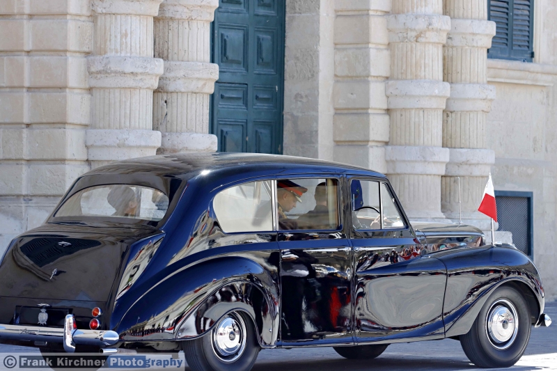 Die Präsidentin im Wagen bei der Abfahrt vom Palast in Valletta zur Kranzniederlegung am Kriegsdenkmal in Floriana. Wenn Sie diese Limousine, eine Austin Princess oder ihr konvertibles Schwestermodell, einmal in Malta sehen, zumal mit Standarte und Eskorte, ist das maltesische Staatsoberhaupt oder ein Staatsgast unterwegs. Oder ein Botschafter ist auf dem Weg zur Akkreditierung. In Valletta ist das eine nicht ungewöhnliche Begegnung, die auch die Aufmerksamkeit von Touristen erweckt. Foto: © Frank Kirchner Photography.