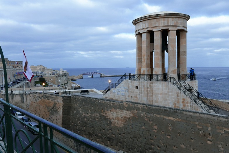 Blick zurück in den Hafen und zur Breakwater Bridge. Im Vordergrund das Siege Bell Memorial, die Friedensglocke, die an die zweite große Belagerung Maltas erinnert. Durch italienische und deutsche Luft- und Seestreitkräfte im Zweiten Weltkrieg. Valletta gehörte zu den am heftigsten bombardierten Städten.